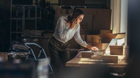Kobieta korzystająca z automatyzacji maili przy biurku, otwarte pudełka, laptop, magazyn w tle.