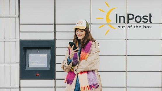 Kobieta stoi przed maszyną Paczkomat InPost, trzyma smartfona dokonując zwrotu towaru w aplikacji InPost Mobile.